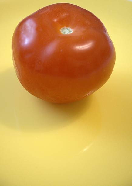 istock One whole tomato on yellow plate close up. 2225819594