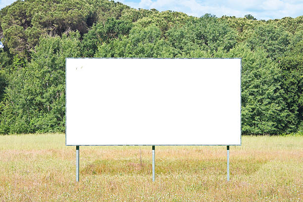 istock Blank advertising signboard in a field with trees on background - concept  with copy space and space for inserting text 2225819773