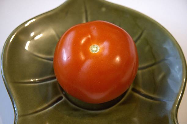istock One whole red tomato on green leaf shape plate. 2225821536