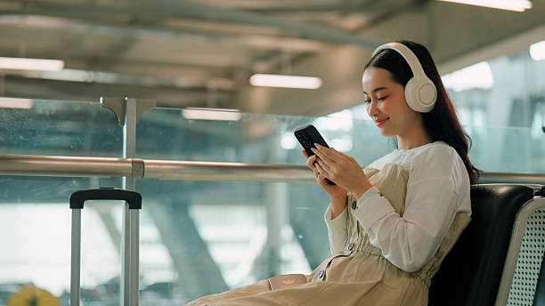 istock Young Asian woman picking music tracks while waiting for her flight boarding time. 2225824106