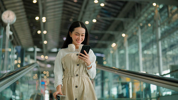istock Young Asian woman using mobile phone and smiling while going down a moving walkway in an airport. 2225824301
