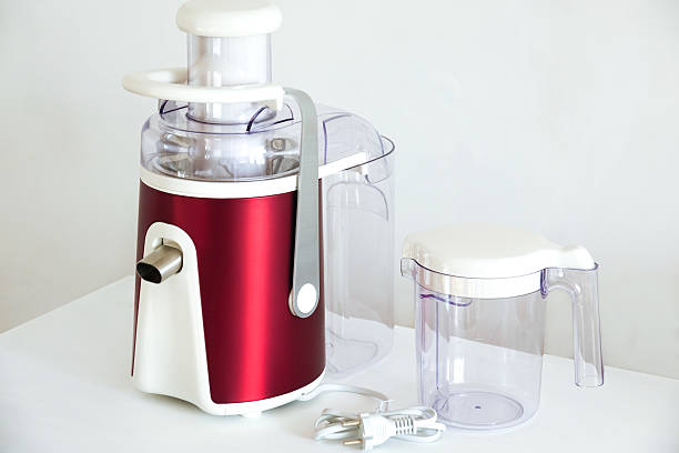 Modern electric juicer with a transparent plastic container and power cord on a white surface. Compact kitchen appliance for making fresh juice and supporting a healthy lifestyle.