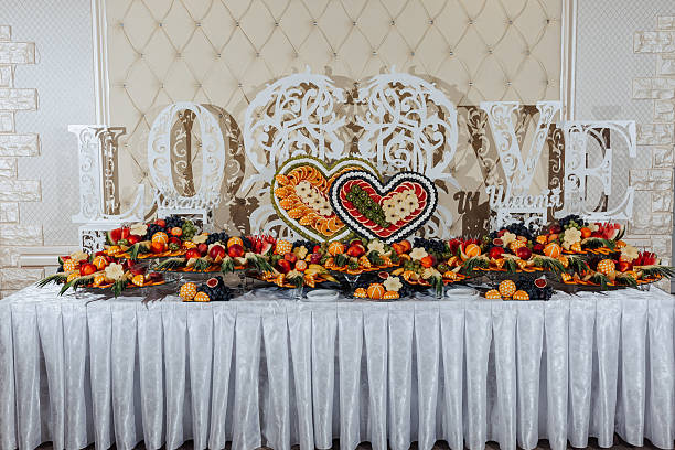 A table with a white tablecloth and a sign that says LOVE. There are many fruits on the table, including apples, oranges, and grapes