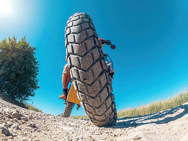 Creative photo of zoomed electric motorcycle wheel with biker on road, low angle view. Arcing horizon with blue sky.