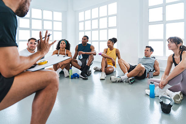 Multiethnic group of sportive people doing functional workout in training class gym group of diverse athletes listening to their personal trainer explaining workout routine during break in modern gym