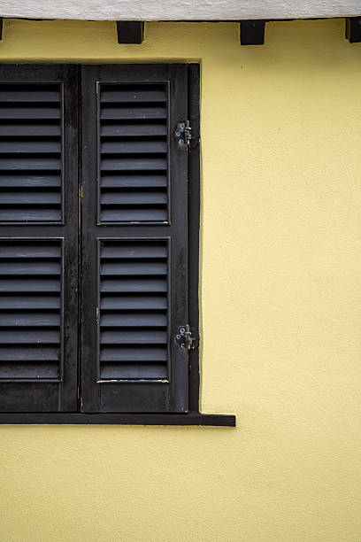 Shutters closed on a residential yellow wall in Bermuda, reflecting colonial architectural influences with clean lines.