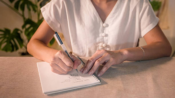 istock Woman writing a list on notebook while sitting at a home table during the day 2225838768