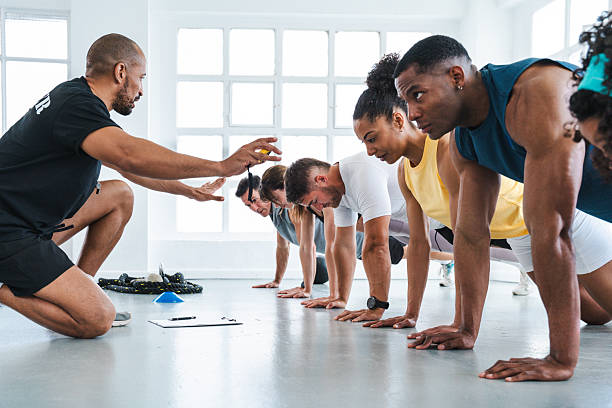 istock Fitness trainer guiding athletes performing plank exercise in gym 2225838885