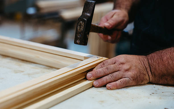 istock Close-up of carpenter hammering wooden window frame in workshop 2225839607