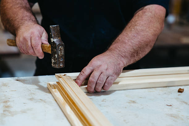 istock Close-up of worker hammering window frame corner during wood assembly 2225839611