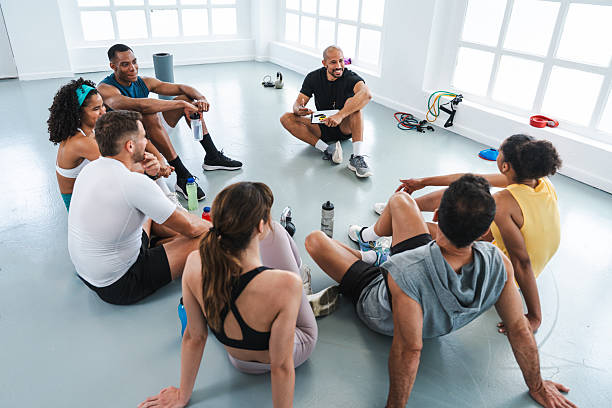 Multiethnic group of sportive people doing functional workout in training class gym multi-ethnic athletes sitting in a circle around their trainer, discussing the day's workout in a bright gym