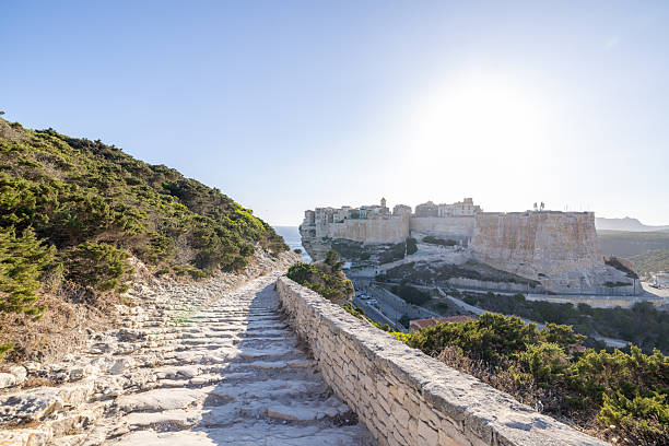 Ancient stone buildings perched on cliffs above the sea in a Mediterranean town. Scenic coastal landscape with winding stone path and lush greenery. Picturesque European travel destination.