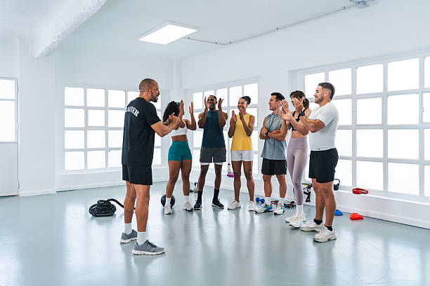 Multiethnic group of sportive people doing functional workout in training class gym smiling multi-ethnic athletes clapping and celebrating their trainer after a successful functional training workout