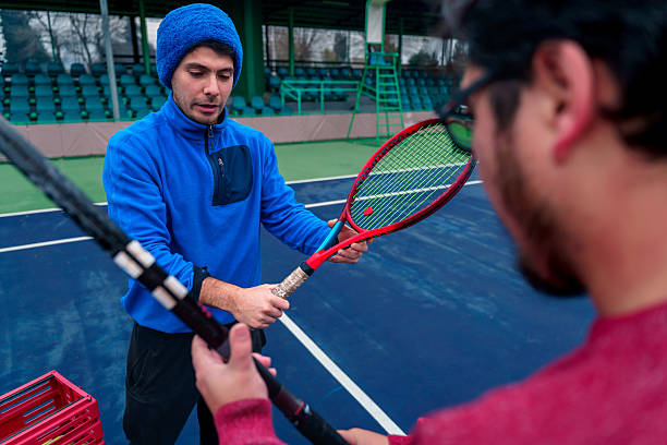 Latin american tennis coach explaining to his student how to correctly hold the racket on a tennis court