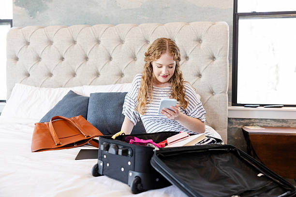 istock Young Woman Packing Suitcase for Trip, Using Smart Phone 2225861475