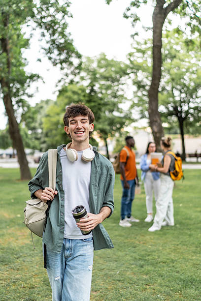 istock Smiling student walking in university campus park with reusable coffee cup 2225861915