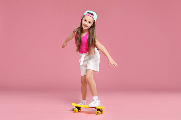 istock Little girl with penny board on pink background 2225863012