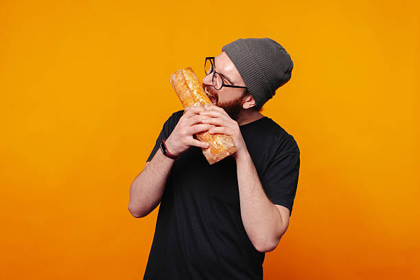 istock A Young Man Playfully Posing with a Baguette in Front of a Bright Orange Background 2225866565