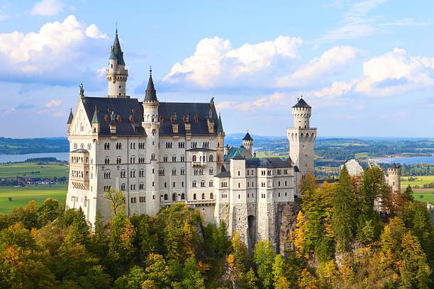 Schwangau, Germany – August 19, 2023: Neuschwanstein Castle in Bavaria, Germany, surrounded by lush greenery under a bright blue sky.