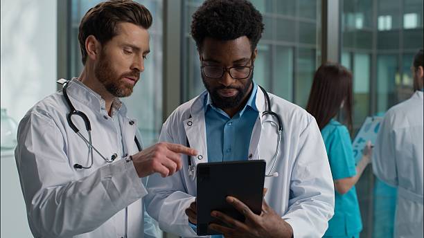 istock Two people men multiethnic doctors talking African American and Caucasian interns uniform labcoat discuss plan for recovery disease rehabilitation using digital tablet together teamwork at hospital 2225883126