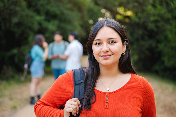 istock Latina student smiling confidently in park with classmates in background 2225888051
