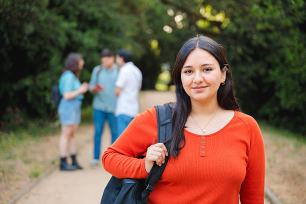 Confident young woman with backpack in park, friends in background