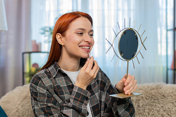 istock Young pretty woman applying makeup looking in mirror smiling while drawing lips with lipstick gently 2225889624