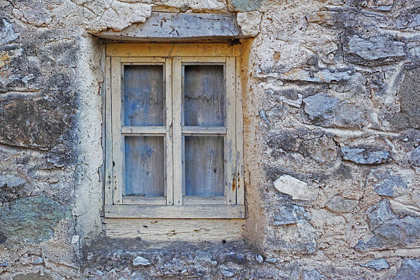 An aged and rustic wooden window frame embedded in a textured, weathered stone wall. The composition showcases the interplay of natural materials, evoking feelings of nostalgia and timelessness.
