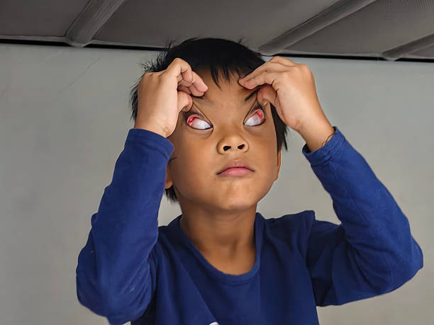Playful child making a funny face by flipping eyelids upward indoors, wearing a blue long-sleeve shirt, showing a humorous and candid childhood moment