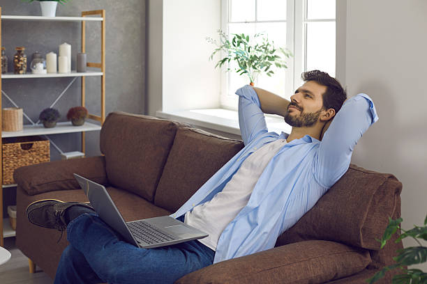 istock Happy young man thinking and dreaming while relaxing on comfortable couch with laptop 2225904802