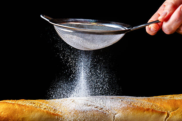 istock Baker sprinkling flour on fresh baguette with a sieve on black background 2225910809