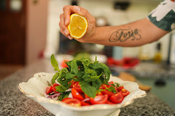 Close-up shot of a hand squeezing lemon juice onto a salad, adding a refreshing citrusy flavor. The scene captures the final preparation step, enhancing the taste and freshness of the salad.