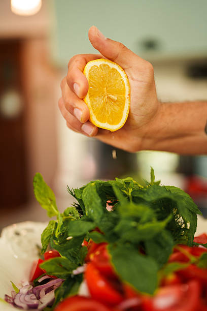 Close-up shot of a hand squeezing lemon juice onto a salad, adding a refreshing citrusy flavor. The scene captures the final preparation step, enhancing the taste and freshness of the salad.