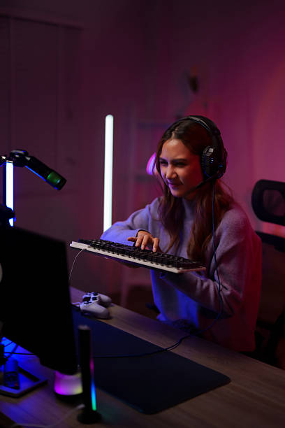 istock Young Asian woman plays computer game streaming online with gaming headset intense concentrated expression on RGB lit desk setup 2225930560