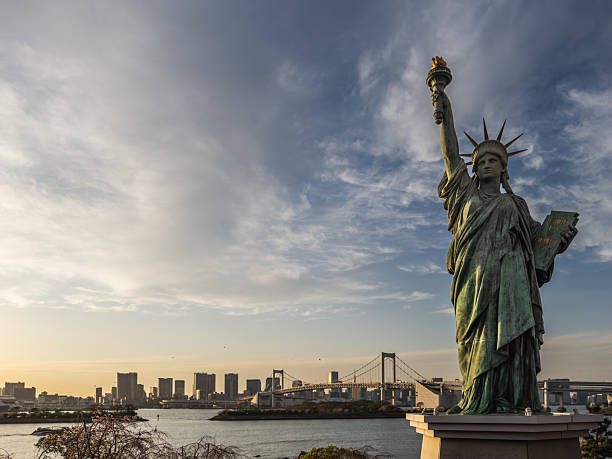 Tokyo, Japan - March 31 2023: Statue of Liberty replica in Odaiba, Tokyo, with Rainbow Bridge and cityscape in the background during sunset.  Iconic landmark, travel destination.