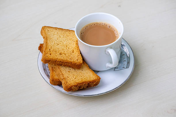 Steaming hot milk tea with delightful bubbles and crunchy rusk biscuits artfully arranged on a wooden backdrop. This inviting drink, known as dudh cha or doodh cha, is ideal for cozy moments.