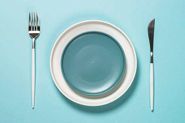 istock Table setting with white plate and cutlery on blue. 2225941271