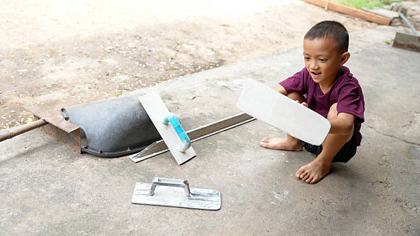 istock Young boy is playing on concrete surface with various tools, including trowel and scoop. His joyful expression reflects curiosity and creativity as he engages with objects around him 2225944152