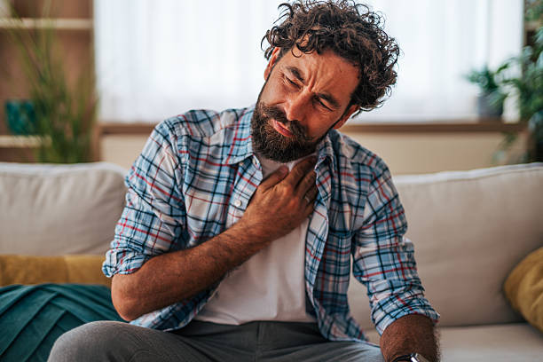istock Man suffering from sore throat at home sitting on sofa 2225944321