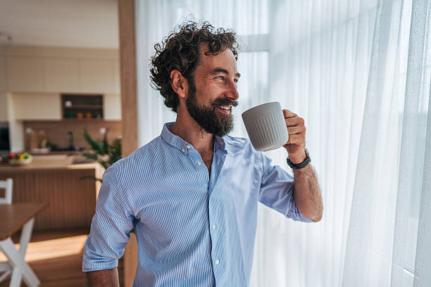 istock Smiling man drinking coffee and looking out the window in his modern kitchen 2225944513