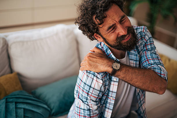 istock Man suffering from shoulder pain while sitting on sofa at home 2225944617