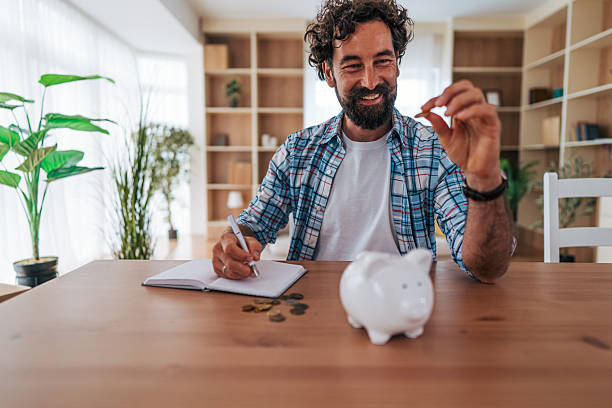 istock Man saving money at home using piggy bank and notebook 2225945135