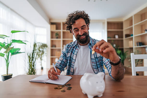 istock Man saving money at home using piggy bank and notebook 2225945240