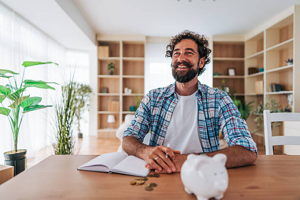 istock Smiling man planning home budget with piggy bank and notebook 2225945241