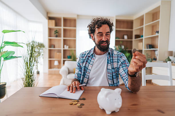 istock Man saving money at home using piggy bank and notebook 2225945242