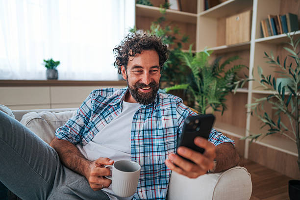 istock Smiling man relaxing on sofa, enjoying coffee and using smartphone 2225945813
