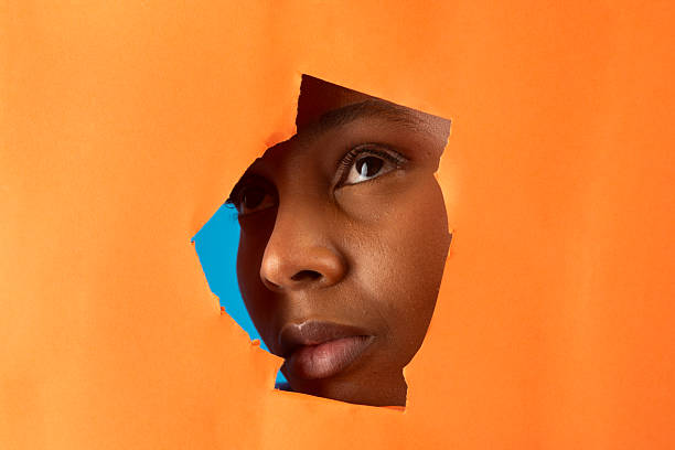 istock Curious black model peeking through orange torn paper on blue background 2225956001
