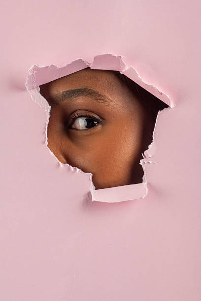 istock Curious black model peeking through torn pink paper 2225956325