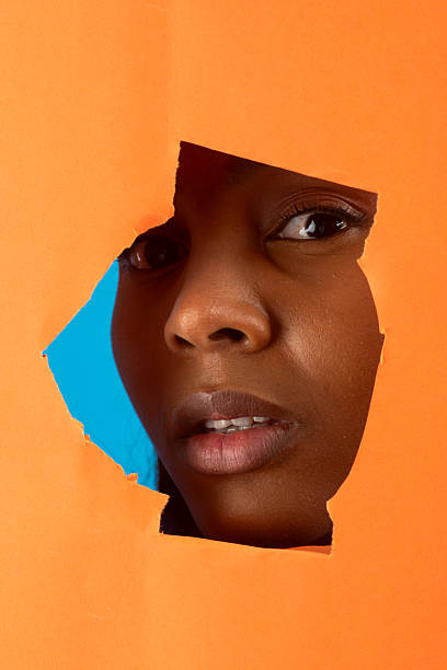 istock Black model peeking through torn orange paper with blue background 2225956878