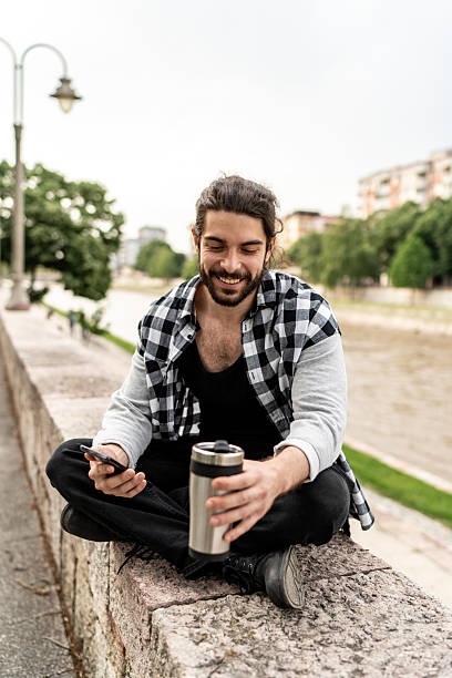 istock Young man enjoying a coffee break by the river, browsing on his smartphone 2225966775